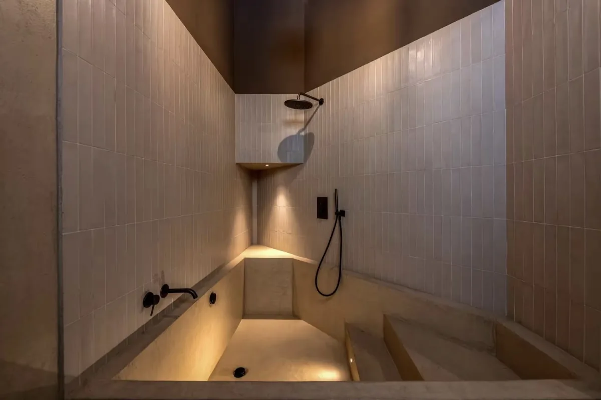 Ambiente bagno con vasca in muratura, doccia e rivestimento chiaro